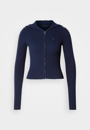 Marinblå ribbad tröja med huva, med dragkedja framtill, långa ärmar och en strukturerad mönstring. Har en liten logotyp på bröstet.