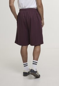 Shorts de sport bordeaux à fines rayures verticales, taille élastique et coupe décontractée. Portés avec des chaussettes blanches à rayures noires et des chaussures foncées.
