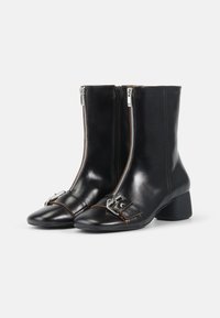 Botas de tobillo de cuero negro con cremalleras laterales dobles, punta afilada y acento de hebilla. El tacón cuadrado proporciona estabilidad. Textura suave en todo.
