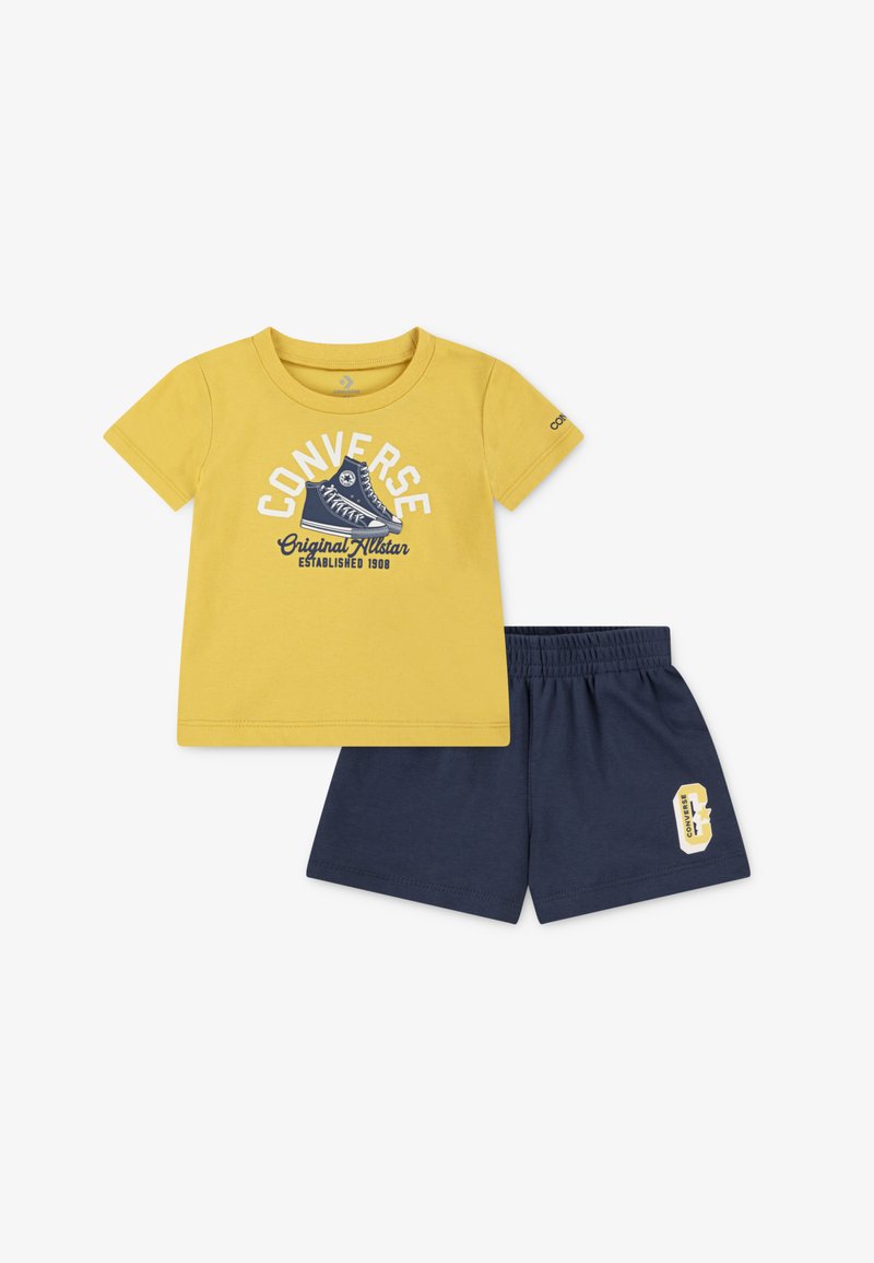 Yellow short-sleeve T-shirt with white and navy graphic logo; paired with navy shorts featuring a yellow logo patch. Soft cotton fabric.
