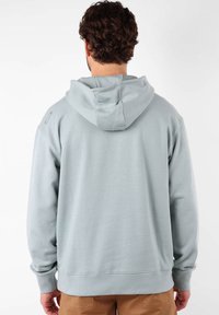Hoodie gris clair en tissu doux, avec une capuche à cordon, des poignets côtelés et une coupe décontractée. Pas de logos ni de motifs visibles.