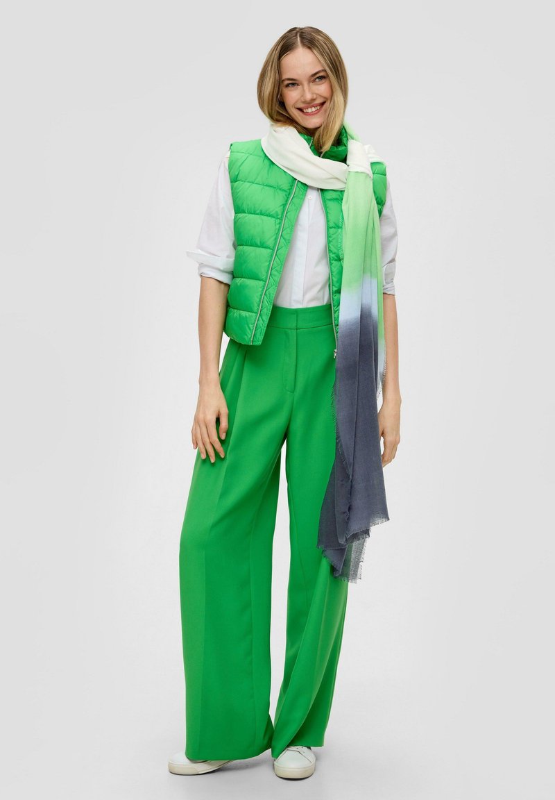 Groene puffer vest, witte shirt, groene wijd-geknipte broek en een gradient blauwe naar groene sjaal. Textuurmaterialen met een gladde afwerking, casual stijl.