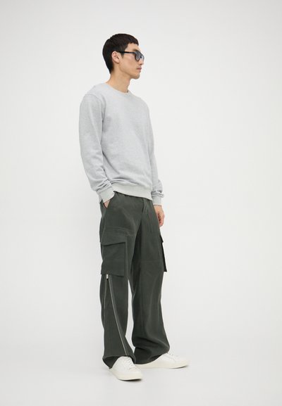 Grey sweatshirt with ribbed cuffs, paired with olive green cargo pants featuring side zippers and multiple pockets. White sneakers.