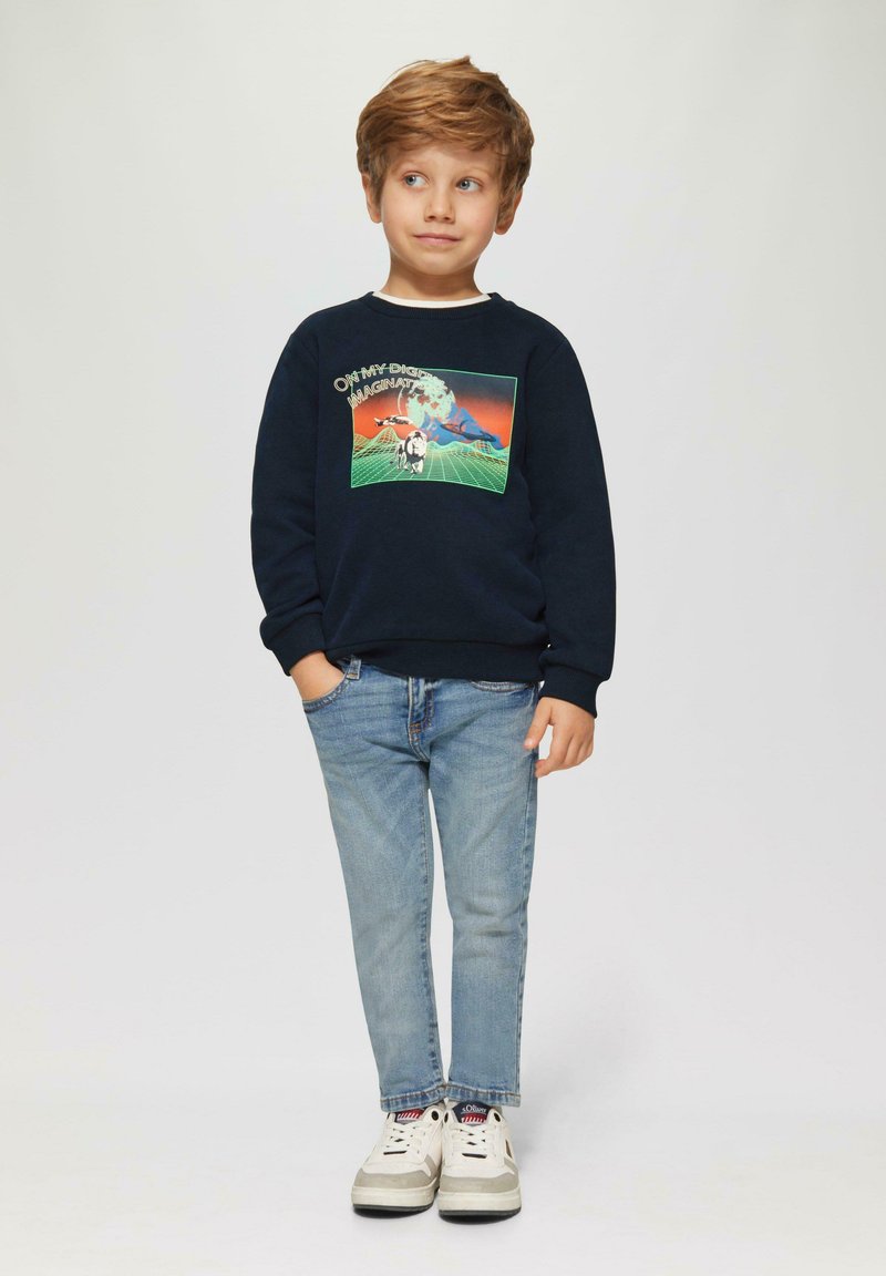 Marineblauer Sweatshirt mit grafischem Druck, hellblaue Jeans und weiße Sneakers. Das Sweatshirt zeigt farbenfrohe Bilder und einen Textdesign.