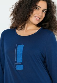 Laivastonsininen pitkähihainen pusero, jossa pyöreä kaula-aukko ja etuosassa teksturoidulla sinisellä huutomerkillä varustettu kuvio. Pehmeä kangas, jossa sileä pinta.