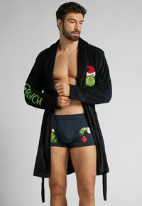 Czarny, pluszowy szlafrok z zielonym motywem Grincha na piersi i rękawach. Do pary ciemnoniebieskie bokserki z grafikami Grincha.