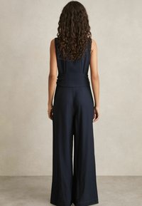 Marine jumpsuit met een wide-leg ontwerp, mouwloos top en geraffineerde taille-details. Glad textuur en effen kleur, minimale hardware.