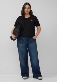 Zwarte katoenen t-shirt met korte mouwen, ronde hals en witte geborduurde details, gecombineerd met wijde blauwe denim jeans en een grijze gebreide tas.