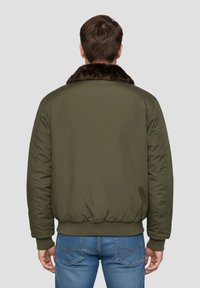 Olijfgroene bomberjack met een bruine bontkraag, geribbelde manchetten en zoom. Het achterkant toont een glad, gewatteerd oppervlak en een eenvoudig ontwerp.