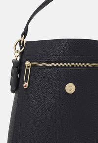 Svart texturerad läderhandväska med ett handtag på toppen, en guldzippered ficka och detaljer i guldmetall, inklusive en dekorativ säkerhetsnål.