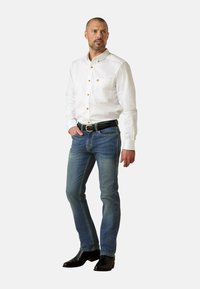 Camisa blanca abotonada con botones dorados y un bolsillo en el pecho; combinada con vaqueros de mezclilla azul claro y botas de cuero negras.