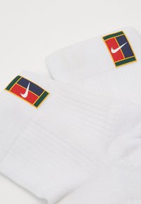 Fehér sportzoknik bordázott textúrával és színes logófoltokkal, piros, zöld és kék szegéllyel, amelyek a Nike emblémáját mutatják.