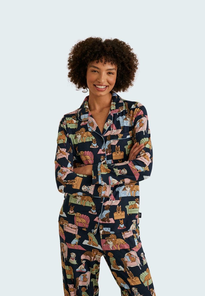 Marineblauw pyjama set met een all-over patroon van geïllustreerde honden op verschillende banken, gemaakt van zachte stof met een klassieke kraag en afgewerkte accenten.