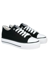 Zapatillas de lona negras con suelas de goma blanca y punteras blancas. Presentan cordones blancos y detalles a rayas en blanco y negro en la lengüeta.