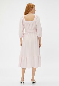 Helles rosa Midikleid mit quadratischem Rückenausschnitt, puffartigen Ärmeln, taillierter Taille und gestuftem Saum. Hergestellt aus strukturiertem Stoff mit glatter Oberfläche.