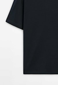 T-shirt noir à manches courtes avec un design uni, coutures visibles sur la manche et l'ourlet, photographié sur un fond blanc.