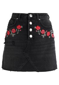 Svart denimkjol med silverknappar, med röd blomsterbroderi på framsidan. Sliten fåll och strukturerad A-linjeform.