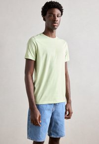Lys grønn bomulls t-skjorte med rund hals og kortermet, med en subtil merkevarelogo på brystet. Brukt sammen med denimshorts.
