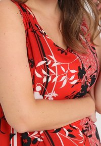 Robe rouge sans manches avec des motifs floraux noirs et blancs, présentant un décolleté en V et une coupe ample, fabriquée en tissu lisse.