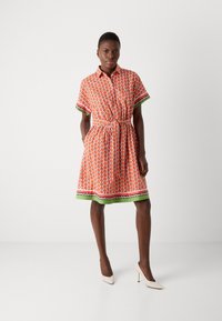 Kurzärmliges Kleid in Orange mit Melonenmuster. Es hat eine taillierte Taille, grüne und rosa Akzente sowie einen knielangen Saum.