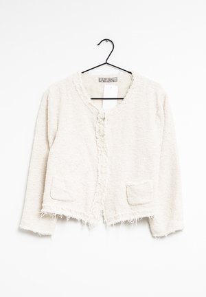 Veste cropped crème en tissu texturé, avec un col rond, des bords effilochés et deux poches avant ; fermée par un seul bouton.