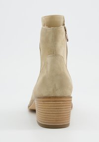 Botines de ante beige con punta redonda, cremallera lateral y un tacón de madera apilada con ranuras horizontales. Textura interior suave.