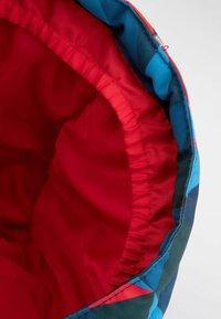 Wielokolorowa torba z tkaniny z czerwoną podszewką, posiadająca wzorzystą zewnętrzną stronę w kolorze niebieskim, zielonym i czerwonym. Miękka tekstura i okrągły kształt.