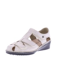Light beige sandal made of soft suede. Features open toe design, adjustable straps, and a low wedge heel with textured soles.