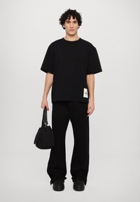 Svart oversized t-skjorte med et logo-patch, parret med løse svarte bukser og en liten svart veske. Glatt tekstur, minimalistisk design.