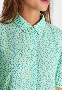 Jasnozielona bluzka z kołnierzykiem, zdobiona wzorem niebieskich kropli. Miękka tkanina i luźne rękawy.