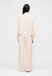 Bež komplet z dolgimi hlačami širokih hlač in puloverjem iz mehkega blaga. Pulover ima visok ovratnik in rebrast rob. Ohlapen kroj zagotavlja udobje.