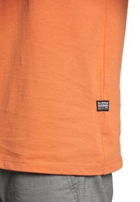Camiseta de algodón naranja con mangas cortas, dobladillo recto y una pequeña etiqueta negra de G-Star Originals en el lado inferior.
