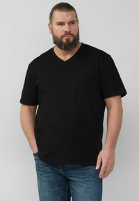 Schwarzes kurzärmliges V-Ausschnitt-T-Shirt aus weichem Stoff. Verfügt über eine lockere Passform und dezente Logodetails auf der Brust. Getragen mit blauen Jeans.