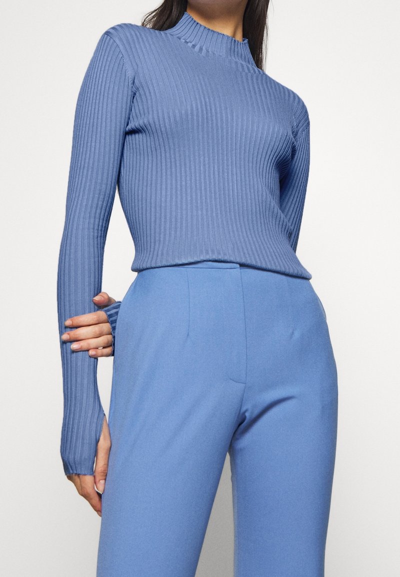Hellblau gerippter Langarmtop mit hohem Kragen, kombiniert mit passenden glatten Hosen. Beide Teile haben eine taillierte Silhouette und eine weiche Textur.