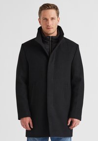 Schwarzer Wollmisch-Mantel mit hohem Kragen und verdeckten Fronttaschen. Er verfügt über ein elegantes, schlankes Design und eine weiche Textur.