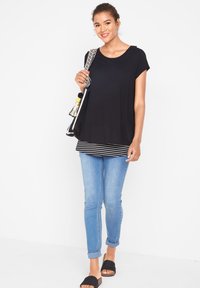 Haut noir à manches courtes avec un ourlet à rayures superposées; associé à un jean bleu clair et des sandales noires à enfiler, portant un sac à motifs.