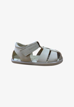 Sandalia de cuero beige con múltiples correas cortadas, cierre de Velcro y suela de goma flexible. Presenta una textura suave y un diseño minimalista.
