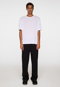 Vit t-shirt med kort ärm i kombination med löst sittande svarta byxor och svarta sneakers. Tyget verkar mjukt och slätt.