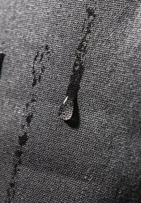 Tela negra resistente al agua con una superficie texturada, mostrando una gota de agua reposando sobre ella y débiles surcos de agua por encima.