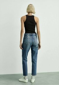 Top sin mangas de canalé negro, jeans de mezclilla azul de talle alto y zapatillas blancas. Enfoque en los detalles de ajuste y textura desde la vista trasera.