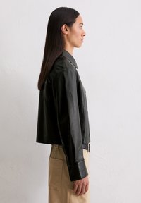 Czarna skórzana kurtka o skróconym kroju z notowanym kołnierzem, zapięciem na guziki i długimi rękawami. Gładka faktura, minimalistyczny design.