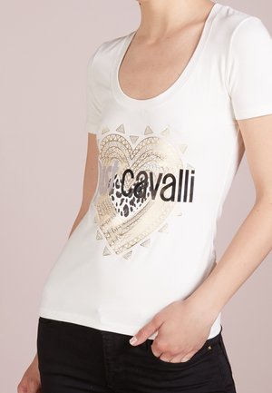 T-shirt blanc à manches courtes avec un design de cœur doré et noir, agrémenté d'accents imprimés animaliers et de motifs géométriques. Texture de tissu lisse.