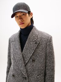 Grau karierter Wollmantel mit doppelt geknöpftem Verschluss, kombiniert mit einem dunklen Rollkragenpullover und einer grauen Mütze, die ein dezentes Logodetail aufweist.