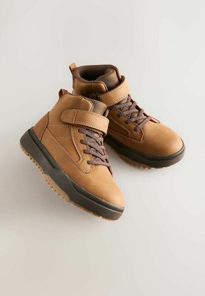 Dzelteni ādas zābaki ar gumijas zoli, ar šņorēm un āķa un cilpas siksnu, ar teksturētām akcentiem un ar mīkstinātu apkārtni komfortam.