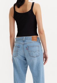 Černý žebrovaný top na tenkých ramínkách, kombinovaný se světle modrými riflemi s vysokým pasem, které mají zadní kapsy a koženou nášivku s logem.