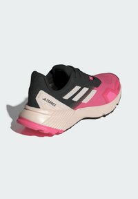 Zapatilla deportiva negra y rosa con una parte superior texturizada, tres franjas blancas y una suela gruesa con un acento rosa en el talón.
