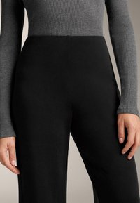 Crne hlače s visokim strukom izrađene od glatke tkanine, uparene s pripijenim sivim rebrastim majicom dugih rukava. Tekstura je mekana i prianjajuća.