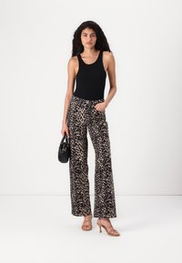Svart uten erme bodysuit kombinert med vide bukser med leopardskrift. Svart håndveske og beige sandaler med stropper fullfører antrekket.