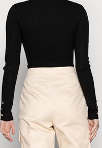 Top negro de manga larga con textura acanalada y corte entallado, combinado con pantalones de talle alto color crema, con bolsillos laterales y puños abotonados.