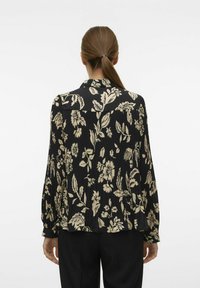 Sort blomsterbluse med glat stof, lange ærmer, krave og plisseret rygdesign med lysebeige blomstermønstre.